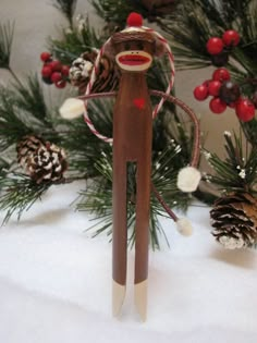 a wooden toy monkey standing in front of some pine cones and christmas tree branches with red berries