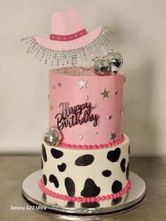 a pink and black birthday cake sitting on top of a silver platter with a cowboy hat