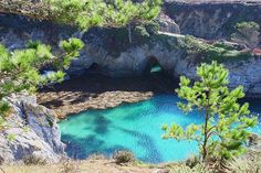 the water is blue and green in this area with rocks, trees, and cliffs