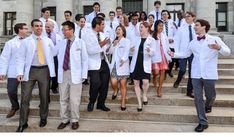 a group of people in white lab coats and ties walking up some steps with their hands together