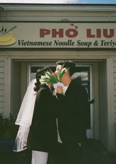 a man and woman kissing in front of a vietnamese noodle shop