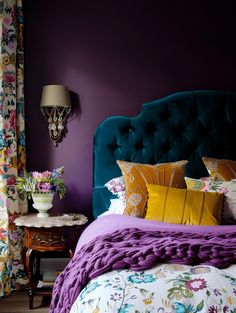 a bedroom with purple walls, floral bedding and colorful pillows on the headboard