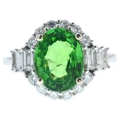 This exquisite ring is a testament to sophistication and refinement. Crafted in 14 karat white gold, it features a stunning 3.04 carat oval-shaped tsavorite as its focal point. The vibrant green hue of the tsavorite is captivating, evoking a sense of natural beauty and elegance. Surrounding the vibrant tsavorite are 18 shimmering round diamonds, totaling 0.69 carats in weight. These diamonds add a touch of brilliance and sparkle to the ring, complementing the rich green color of the tsavorite pe Brilliant Cut Oval Diamond Ring With Tsavorite, Oval Tsavorite Diamond Ring For Formal Occasions, Oval Tsavorite Rings With Halo Setting, Classic Oval Tsavorite Ring, Classic Oval Tsavorite Emerald Ring, Oval Tsavorite Ring In White Gold, Oval Tsavorite Ring With Center Stone, Oval Tsavorite White Gold Ring, Oval Tsavorite Diamond Ring In Green