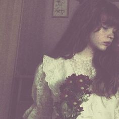 a woman with long hair wearing a white dress and holding a bouquet of flowers in her hand