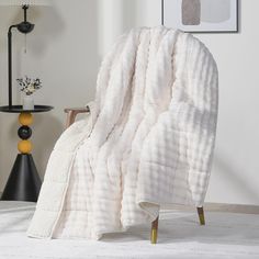 a white blanket sitting on top of a wooden chair next to a lamp and table