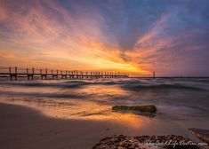 the sun is setting over an ocean with a pier in the distance