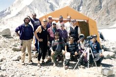 a group of men standing next to each other in front of a tent on top of a mountain