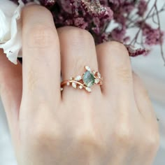 a close up of a person's hand with a ring on their finger and flowers in the background