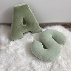 two pillows sitting next to each other on top of a white rug in front of a letter shaped pillow