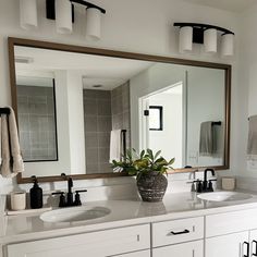 a bathroom with two sinks and a large mirror on the wall above it is also a potted plant