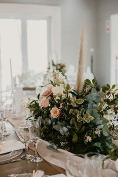 an arrangement of flowers and greenery sits on the dining room table at this wedding reception