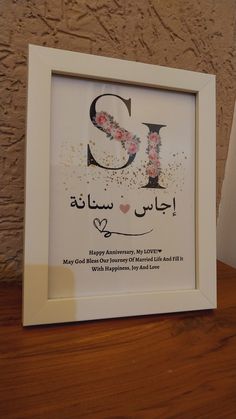 a white frame with the letter s in arabic and flowers on it, sitting on a wooden table