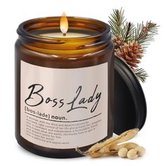 a candle that is next to some pine cones and a tin with the words boss lady on it