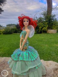 the little mermaid doll is sitting on top of a rock in front of some grass