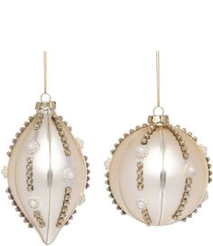 two white and gold christmas ornaments hanging from the back of each ornament, with beaded trimmings