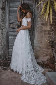 a woman standing in front of an open door wearing a white wedding dress with off the shoulder sleeves