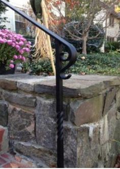 an iron handrail on the side of a stone wall with flowers and trees in the background