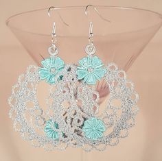 a pair of blue and silver earrings with flowers on them sitting in front of a glass vase