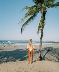 a woman standing on top of a sandy beach next to a palm tree in front of the ocean