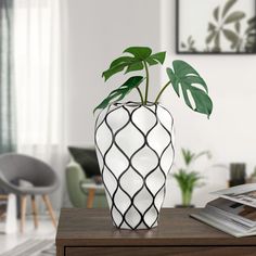 a white and black vase with a green plant in it sitting on a wooden table