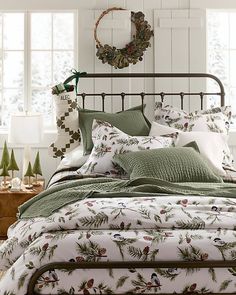 a bed with green and white comforters in a bedroom next to two christmas wreaths