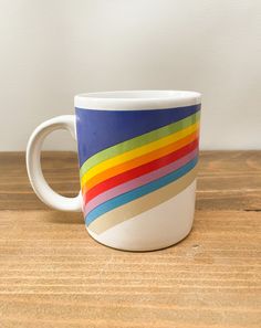 a white coffee cup with multicolored stripes on the outside and inside, sitting on a wooden surface