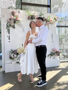 a man and woman standing next to each other in front of a wall with flowers