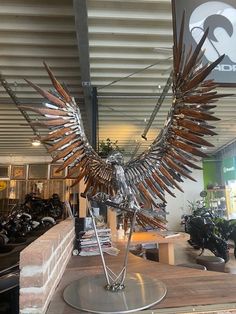 a metal bird sculpture sitting on top of a wooden table next to a store sign