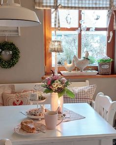 a white table topped with plates and cups filled with food next to a window covered in wreaths