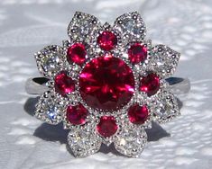 "This is a beautiful and striking MARIGOLD ring, featuring lab rubies and moissanites, set in white gold floral filigree that looks like sparkly lace on your finger! The center stone is a 6.5mm lab ruby. It is set in my MARIGOLD ring, featuring a delicate milgrain bezel surrounded by two rows of petals with floral filigree. The inside row of petals is made with lab rubies and outside petals hold moissanites. The gallery is designed to be completely open, making the ring very comfortable and easy Aquamarine Engagement Ring White Gold, Delicate Engagement Ring, Floral Filigree, Moissanite Bridal Sets, Gold Lotus, Sparkly Ring, White Gold Diamond Engagement Ring, Aquamarine Engagement Ring, Engagement Ring White Gold