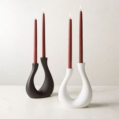 two white and black vases sitting next to each other with red candles in them