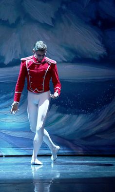 a man in red jacket and white pants on stage