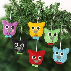 four felt cat ornaments hanging from a christmas tree with green branches in the foreground