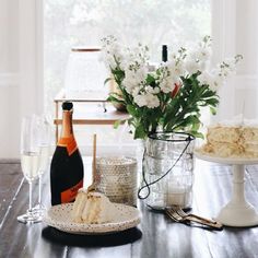 a table with cake, wine and flowers on it in front of a window sill