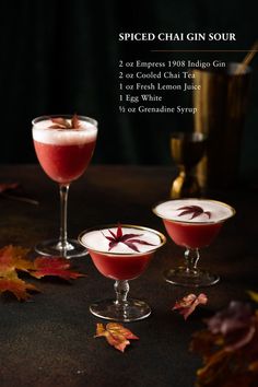 two glasses filled with liquid sitting next to each other on top of a table covered in autumn leaves