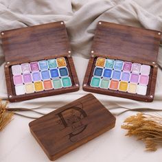 two wooden trays filled with different colored paints on top of a white bed next to each other