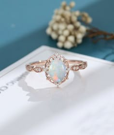 a white opal and diamond ring sitting on top of a blue table next to flowers