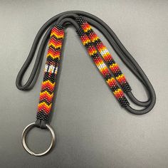 an orange, yellow and black beaded lanyard with a metal ring on a gray surface