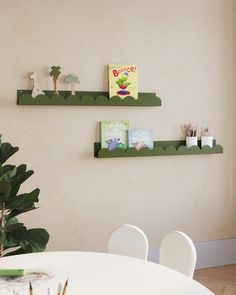 two green shelves on the wall above a white dining room table with chairs and a potted plant