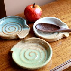 three ceramic bowls with spoons and an apple on a wooden counter top, one is empty