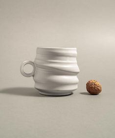 a white coffee cup with a walnut in the middle next to it on a gray surface