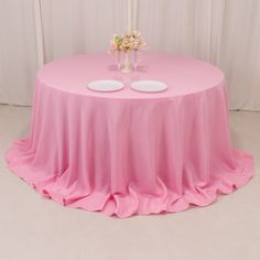 a pink table with two white plates on it and flowers in vases at the top