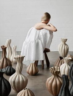 a woman sitting on a chair in front of many vases with her arms crossed