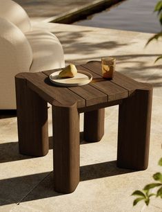 a small wooden table sitting on top of a patio next to a white chair and potted plant