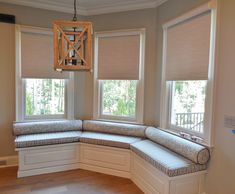 a corner window seat in the middle of a room with three windows and a light fixture hanging from the ceiling