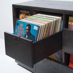 a record player's storage unit with vinyl records in the drawer and an album on top