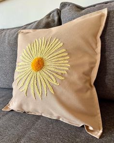 a pillow with a yellow flower embroidered on the front and back of it, sitting on a couch