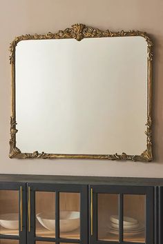 an ornate gold framed mirror on the wall above a china cabinet with plates in it