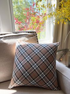 a plaid pillow sitting on top of a couch next to a vase with yellow flowers