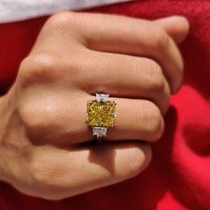 a woman's hand with a fancy yellow diamond ring on her left hand, and a red blanket in the background